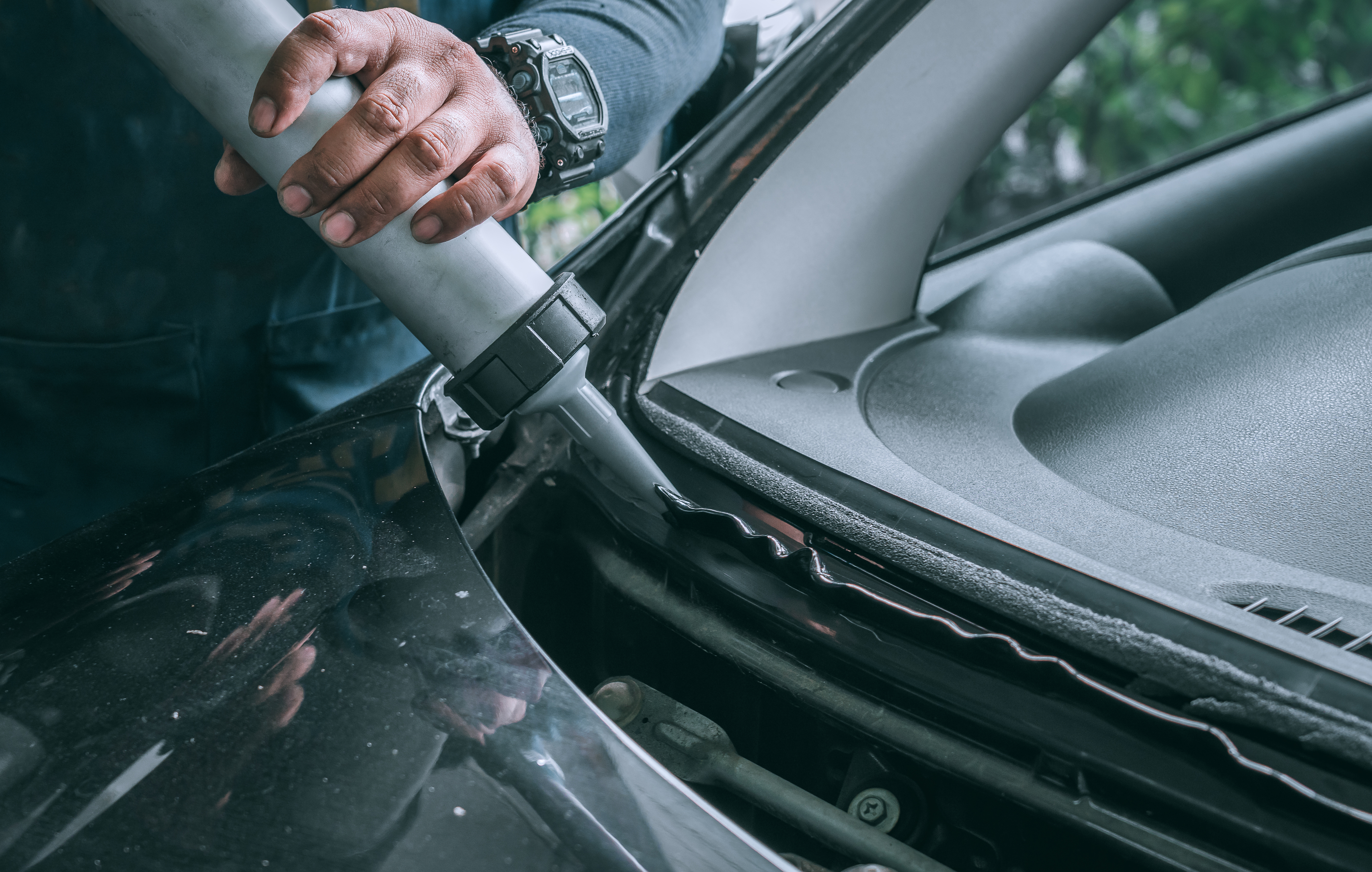 Automobile glazier adding glue on windscreen or windshield of a car in auto service station garage before installation